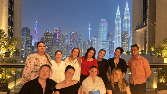 New Zealand health and beauty entrepreneurs in Kuala Lumpur, Malaysia, with the Petronas Twin Towers illuminated behind them.